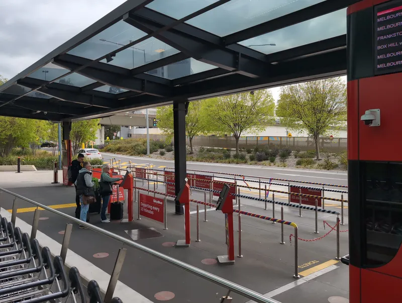 The SkyBus stop at Terminal 4 — buy at the red self-service kiosk, then queue along the rails