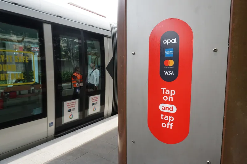 Opal reader at a light rail stop. The panel lists Opal, American Express, Mastercard and Visa — tap here before you board.