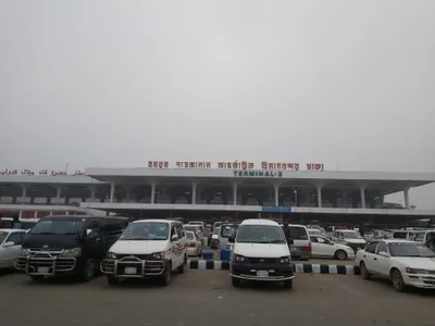 The front of Terminal 2 — the forecourt fills with white microbuses and cars. You find the car you booked by matching its plate against the app.
