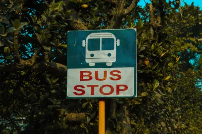 The stop sign carries only a pictogram and the words "BUS STOP" — no place name, no route number — so you identify your bus from the Bengali board on its front.
