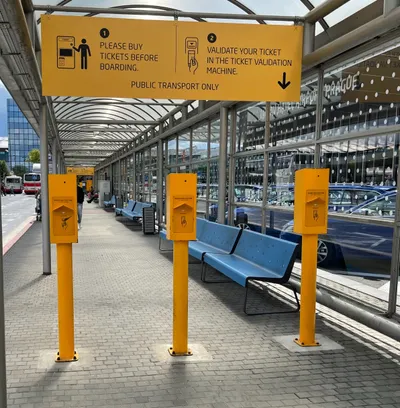 The bus stop at Terminal 1 - the yellow posts are the validators, and the banner gives two steps: "1. Please buy tickets before boarding. 2. Validate your ticket in the ticket validation machine."