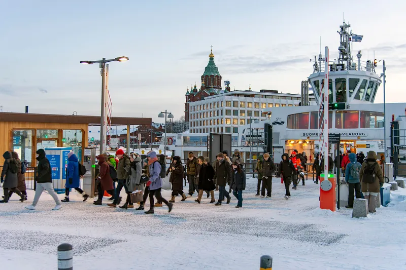 The pier on the east side of the Market Square: the white ferry lettered SUOMENLINNA · SVEABORG lies beyond the wooden pavilion as passengers come ashore, with Uspenski Cathedral behind.