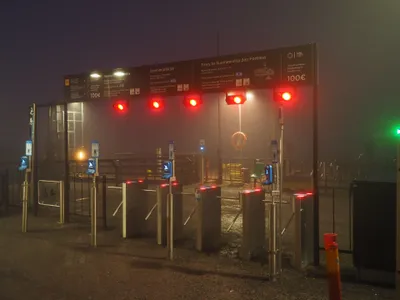 Tripod gates line the entrance to the pier. The sign reads: beyond this point you must hold a valid ticket, Suomenlinna needs zones A and B, penalty fare €100 — and you pass through when the light turns green.