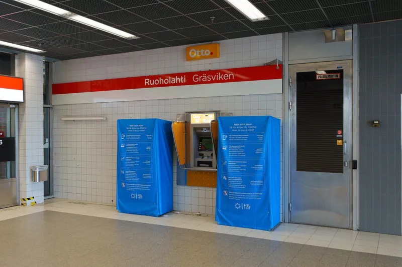 Ruoholahti station entrance, August 2026: the withdrawn large ticket machines are wrapped in HSL's own "How to buy a ticket" cover — the app, the online store, contactless at card readers, and sales points.