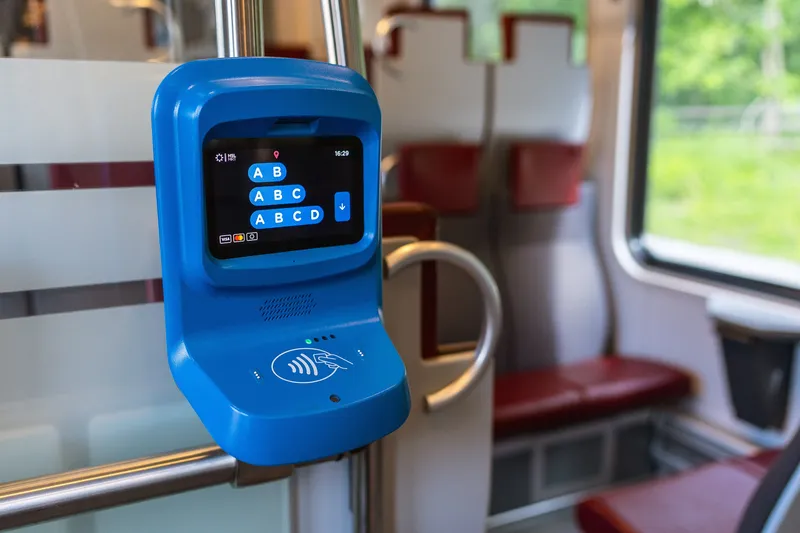 The card reader inside a commuter train — choose the zones (AB, ABC, ABCD) on the screen, then hold your card to the contactless symbol below. The Visa and Mastercard marks are at the bottom left of the screen.