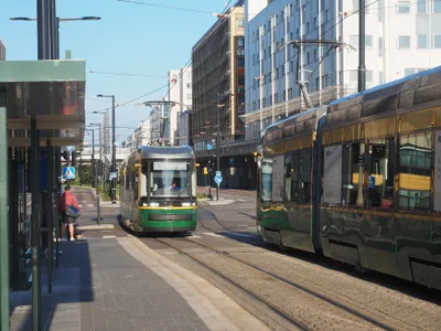 A Helsinki tram pulling into a street-side stop — green and yellow, with the line number and destination shown on the front.