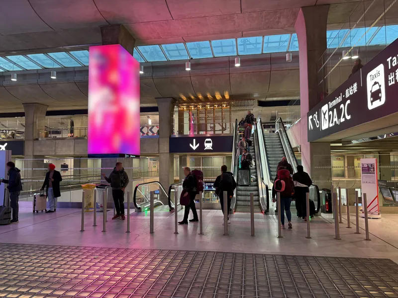 The station concourse at CDG Terminal 2 — the black overhead sign with a downward arrow and a train points to the platforms, and "Taxis" is signposted to the right.