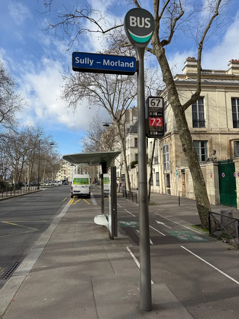 バス停のポール。丸い「BUS」標識の下が停留所名、その下のパネルに系統番号と行き先、右に待ち時間の分数が出る（67系統がPalais Royal行きで1分、72系統がParc de Saint-Cloud行きで4分）