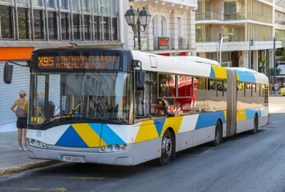 The airport express bus — its front display reads "X95 Syntagma Express Athens Airport"