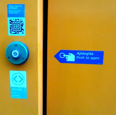 ドアの外側に貼られた「Please scan your mobile ticket」のQRコード。アプリの券はここを読み取って有効化する。すぐ下は「Ajtónyitó／Door opener」ボタン