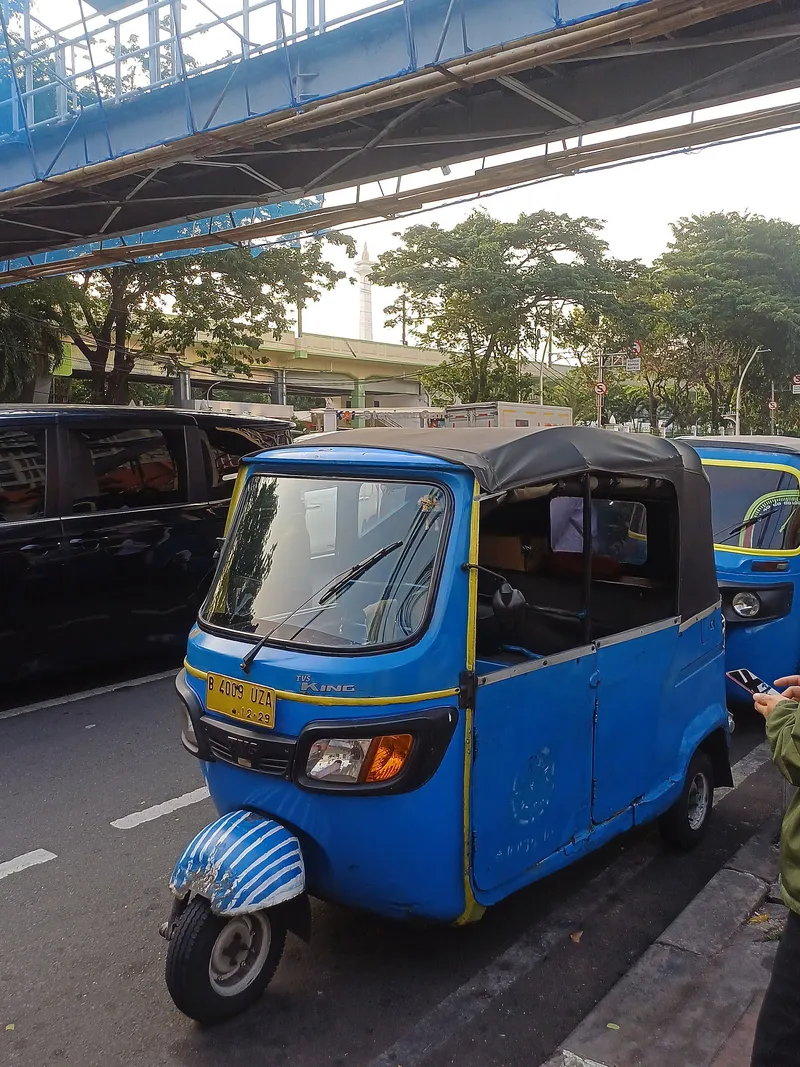 A blue bajaj in central Jakarta, with the Monas obelisk behind