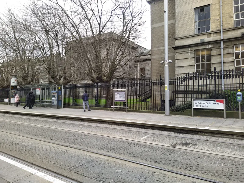 The platform at the Four Courts stop: one ticket machine under the shelter, with the red-banded stop name sign and a validator to the right. There are no gates anywhere.