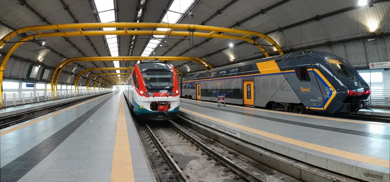 Two kinds of train side by side at the airport station — the Hitachi "Rock" on the right is a regional (REGIONALE) service to Roma Ostiense