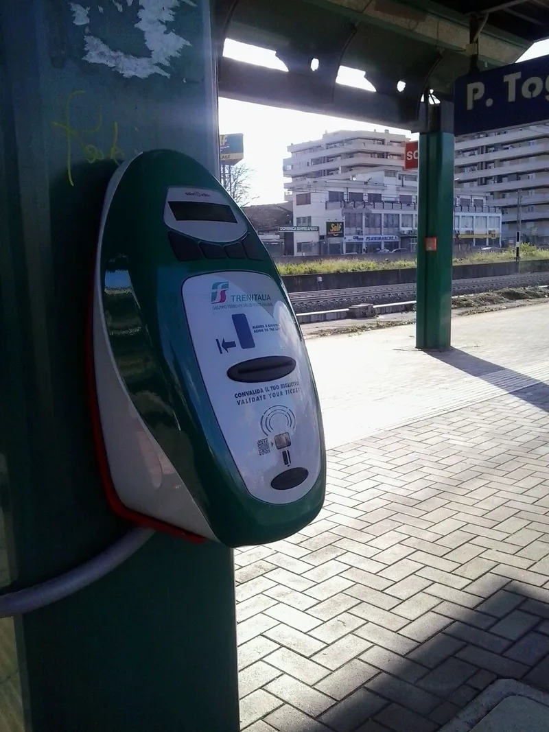 A platform validator marked "CONVALIDA IL TUO BIGLIETTO / VALIDATE YOUR TICKET" — Trenitalia tickets go in here