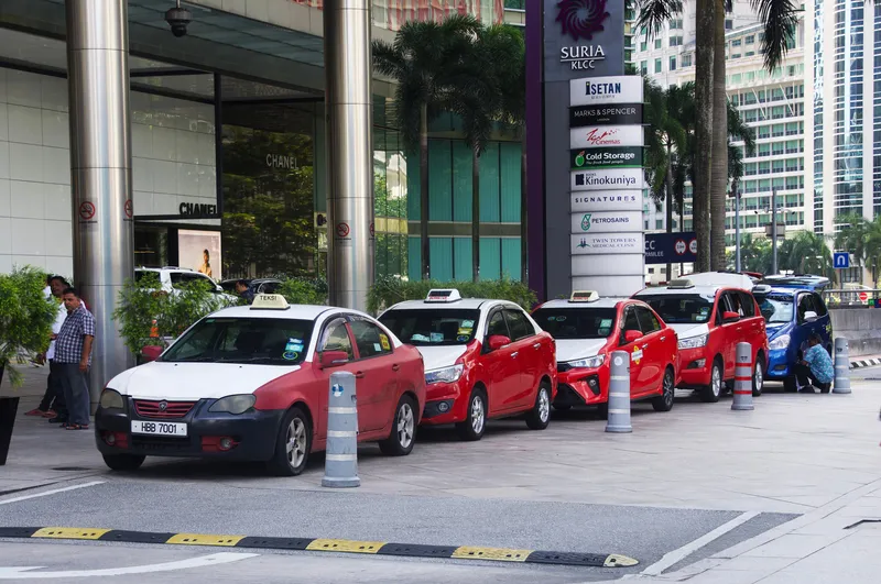 The taxi rank outside Suria KLCC — red-and-white street taxis with TEKSI BERMETER roof signs; the blue one at the right is a different class, its roof sign reading EXECUTIVE