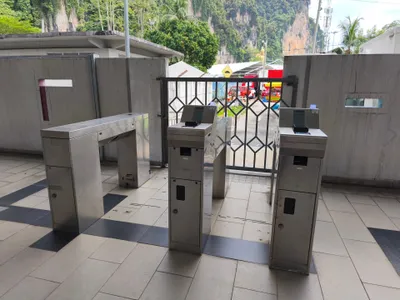 Fare gates at Batu Caves — the flat pad in front of the screen is where you tap your card; the black block above it reads QR codes