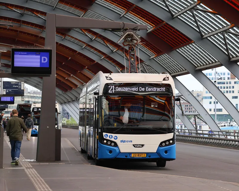 The upper bus station at Amsterdam Centraal. GVB buses are white and blue, with the line number and destination on the front.