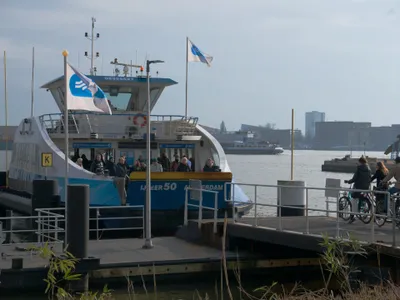 A ferry coming alongside a landing in Amsterdam-Noord. Passengers wait on the pier with their bikes and board once everyone has stepped off.