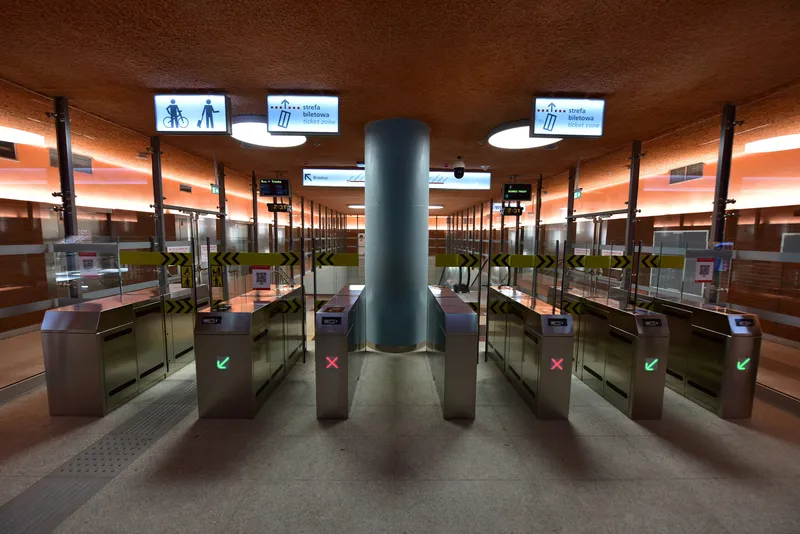 Fare gates at Bemowo station. The lit "strefa biletowa / ticket zone" signs mark where the paid area begins — have a ticket before you pass.