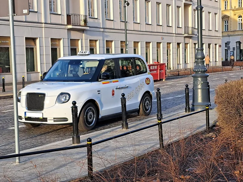 A licensed Warsaw taxi: the roof TAXI sign, the side number inside the yellow-and-red stripe, and the city crest on the door.
