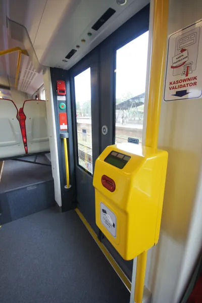 Inside an SKM train: push your paper ticket into the yellow validator by the door. The wall sign reads "KASOWNIK / VALIDATOR".