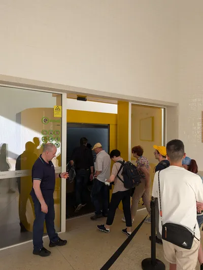 The lower station of the Graca funicular. A staff member works the door while passengers board in a queue behind a belt barrier.