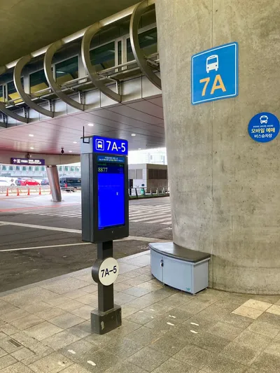 A bus bay outside the terminal. The 7A on the pillar and 7A-5 on the post are the bay numbers, and the screen shows the next departure's route number.