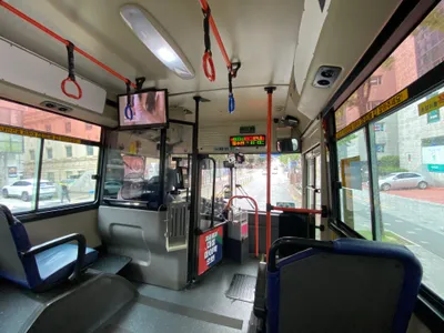 The front of the bus. The overhead LED keeps scrolling 하차시 태그안내 / 필수!! - tapping off when you get out is required. The box beside the driver is the farebox.