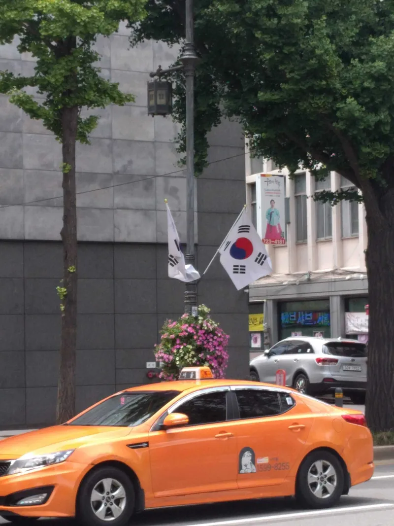 An orange taxi in Seoul's standard livery, 서울 on the roof light. Whether it is free is shown on the red display inside the windscreen.