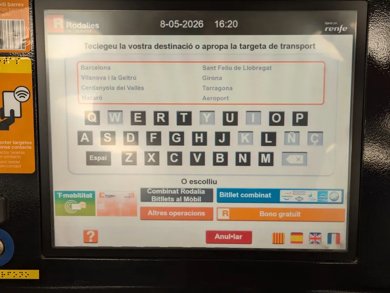 Rodalies ticket machine: type your destination or tap your transport card. The flags at bottom right switch the display language — the Union Jack for English.
