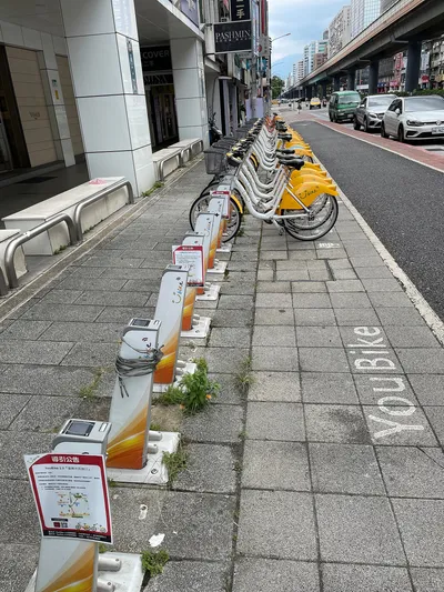 A YouBike station in Taipei — low docking posts along the pavement, "YouBike" painted on the ground