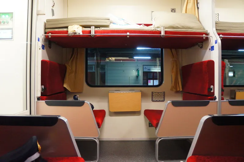 An intercity second-class sleeper — bedding stacked on the upper berth, facing seats below