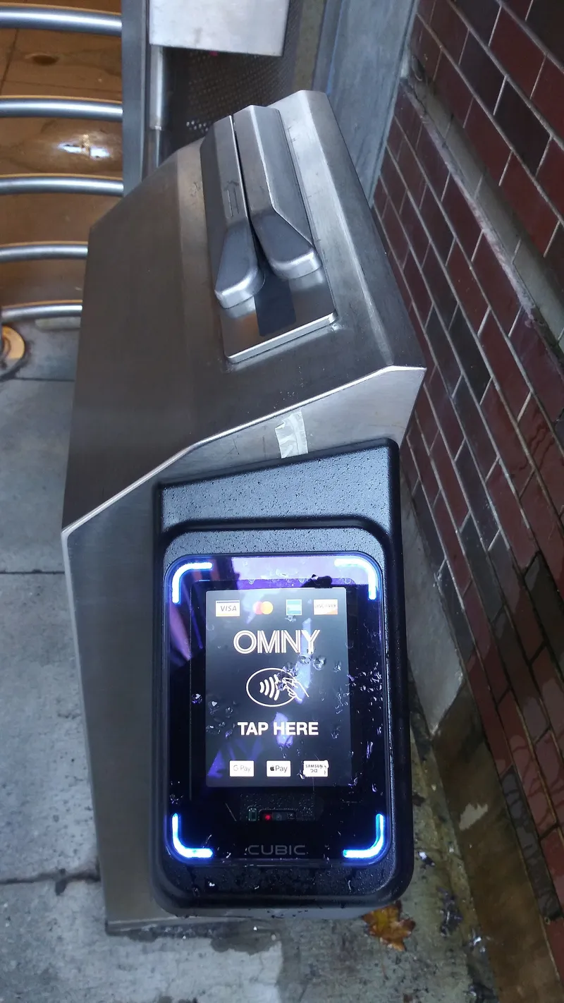 OMNY reader on a subway turnstile — hold a contactless card or phone against the "TAP HERE" panel