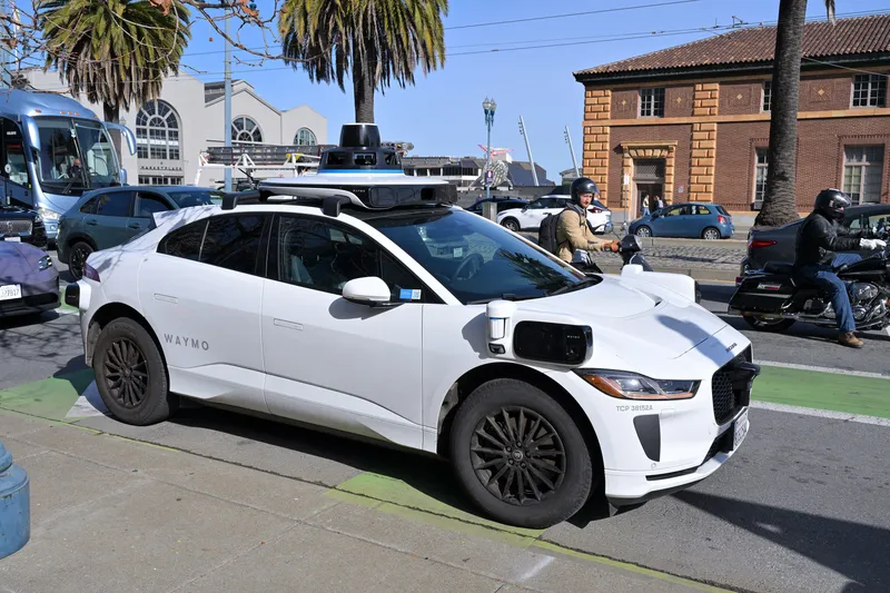 A Waymo self-driving car (Jaguar I-Pace) in San Francisco — 'WAYMO' on the door, sensors on the roof and corners